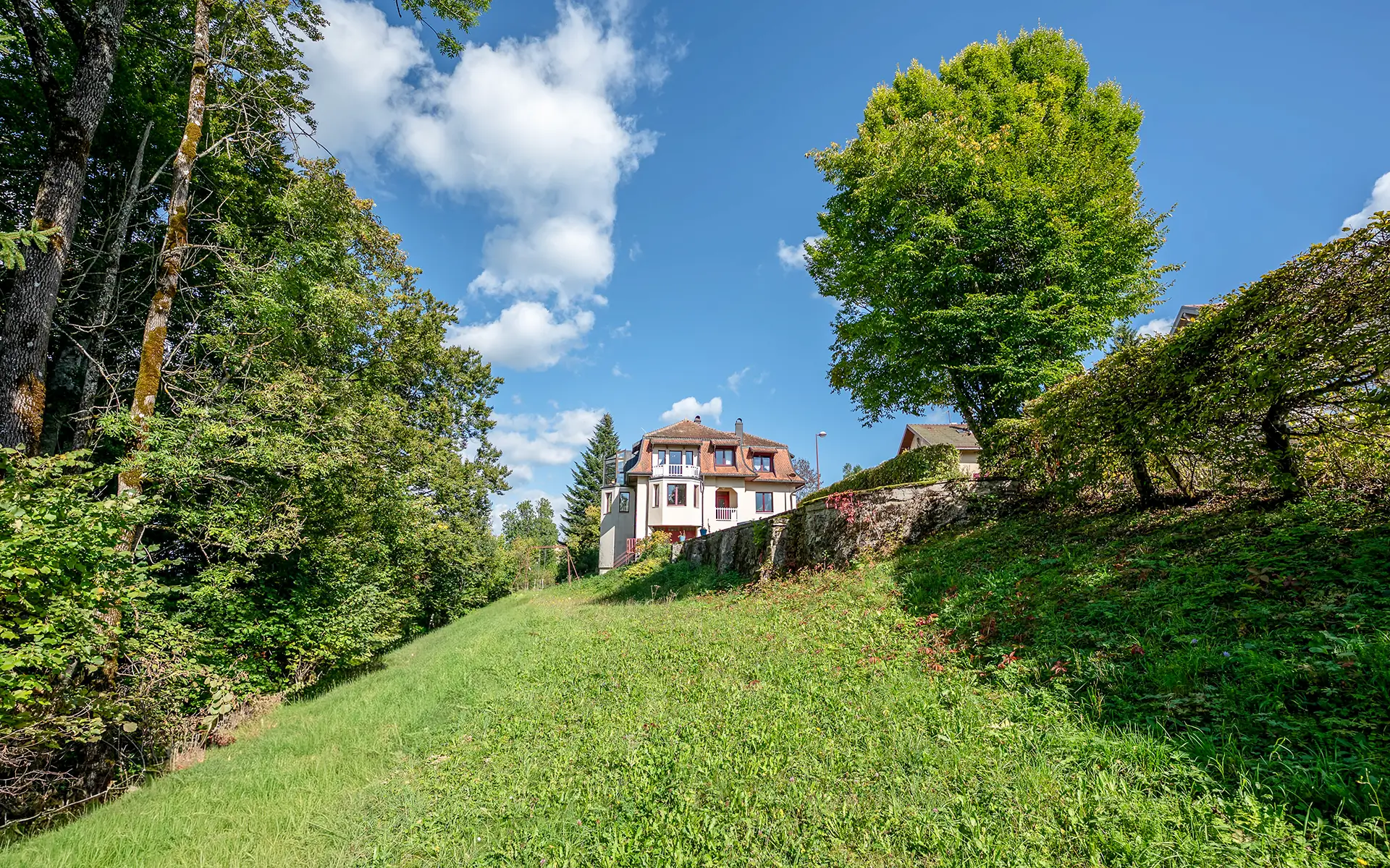 Jardin et façade de la maison des années 30 à Malbuisson avec vue lac à vendre - Arrière-Cour, agence immobilière spécialisée dans le Doubs