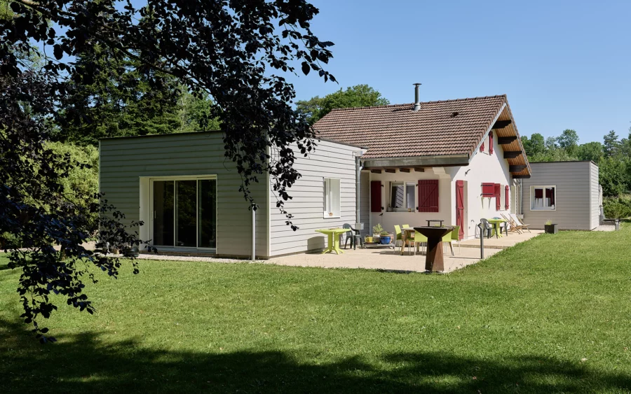 Façade et verdure de la maison de famille à l'orée de la forêt de Chaux à vendre - Arrière-Cour, agence immobilière spécialisée dans le Jura