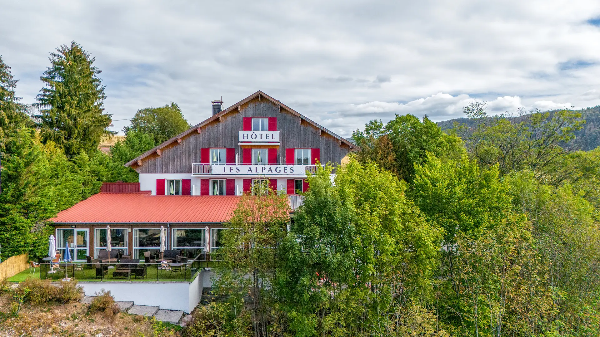 Façade et verdure de l'hôtel ouvert sur les forêts du Jura à vendre - Arrière-Cour, agence immobilière spécialisée dans le Jura