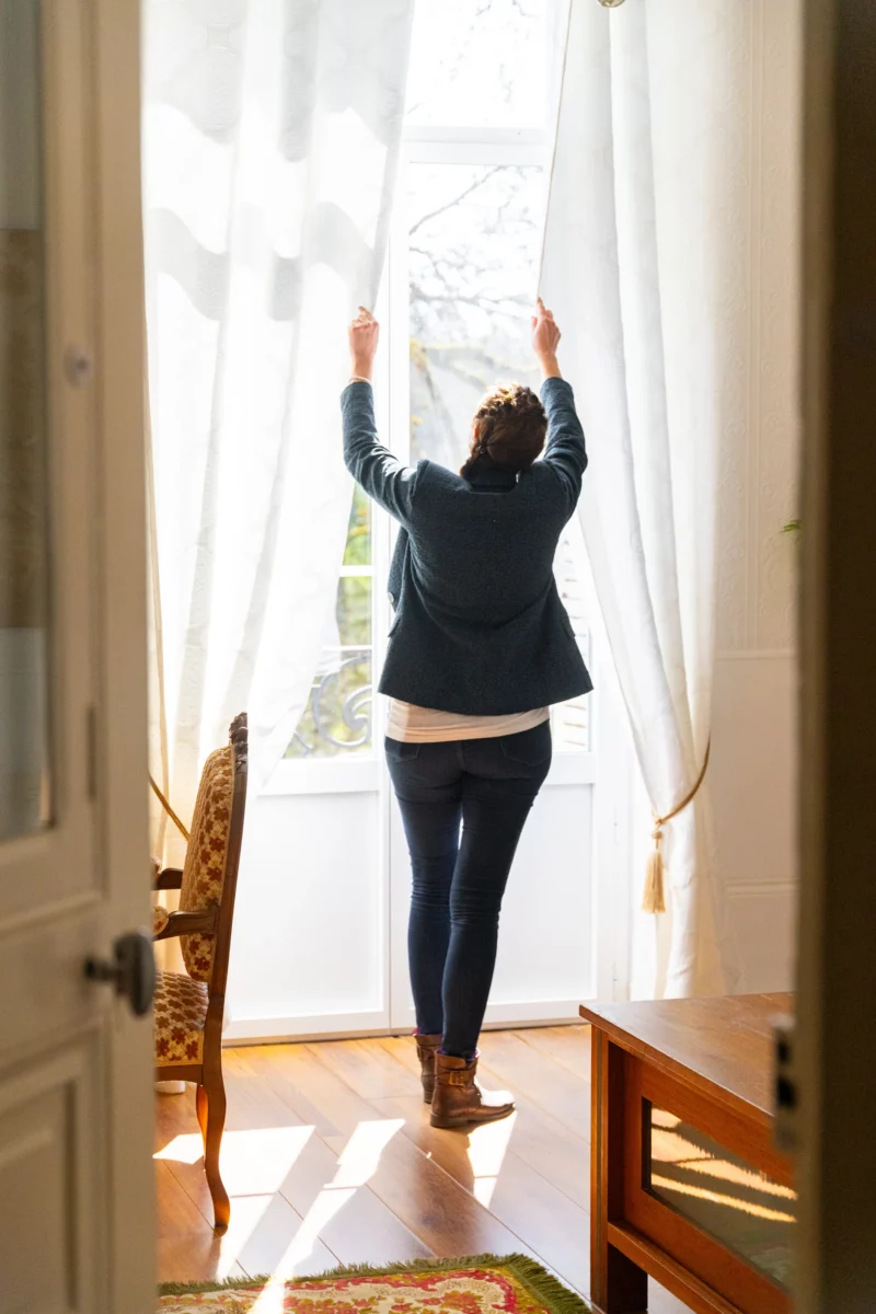 Conseillère immobilière ouvrant les rideaux d’une pièce lumineuse lors de la visite d’un appartement de caractère.
